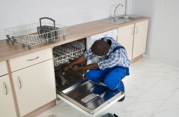 A technician in blue overalls works on a dishwasher, highlighting kitchen appliance repair services in Las Vegas, NV.