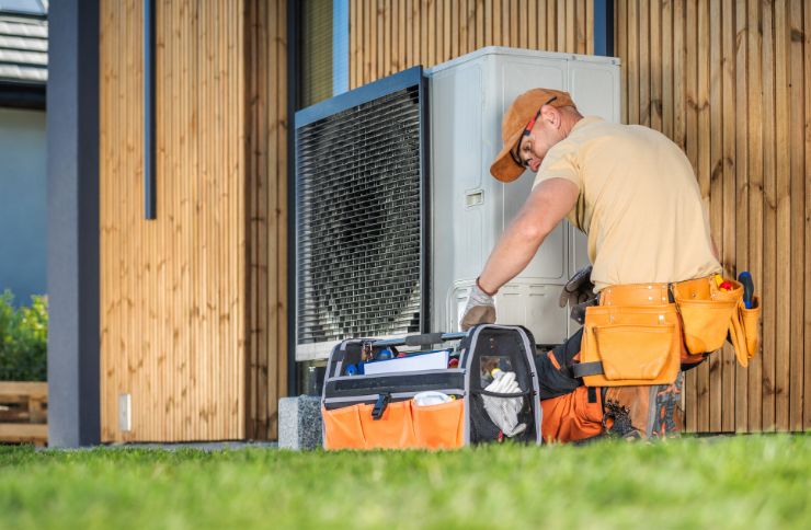 A worker in a hard hat repairs an air conditioner, illustrating heating and cooling services in Las Vegas, NV.