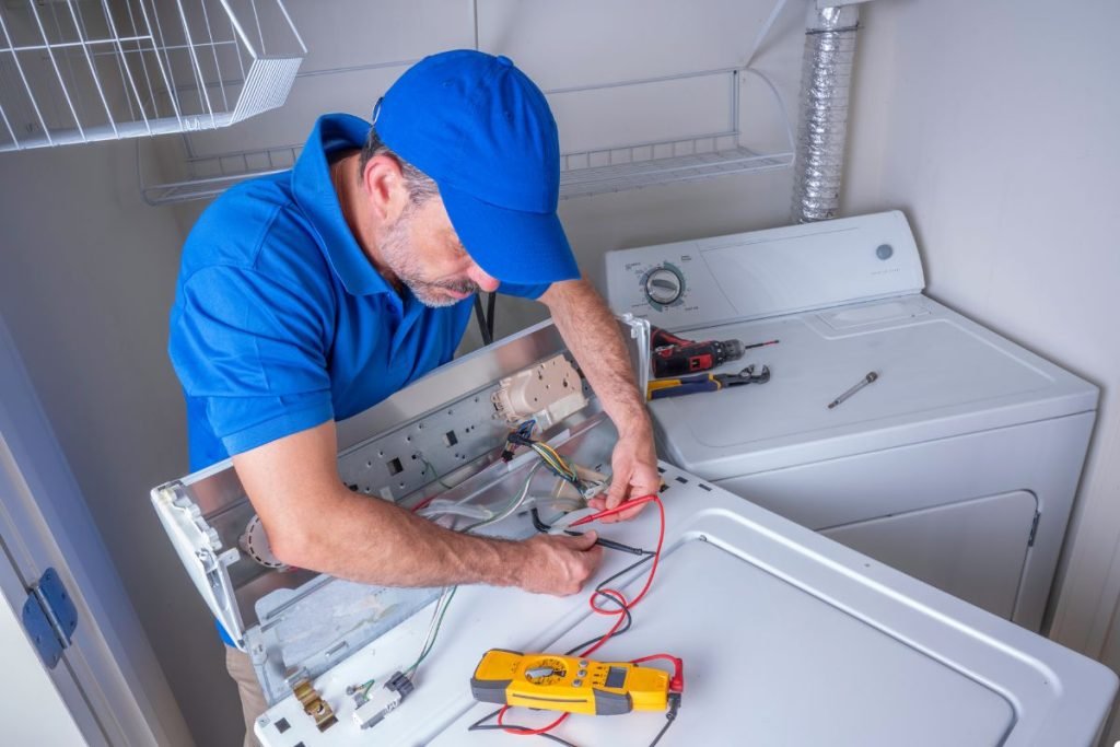 A man wearing a blue shirt is engaged in fixing a washing machine, demonstrating his technical skills in a laundry setting.